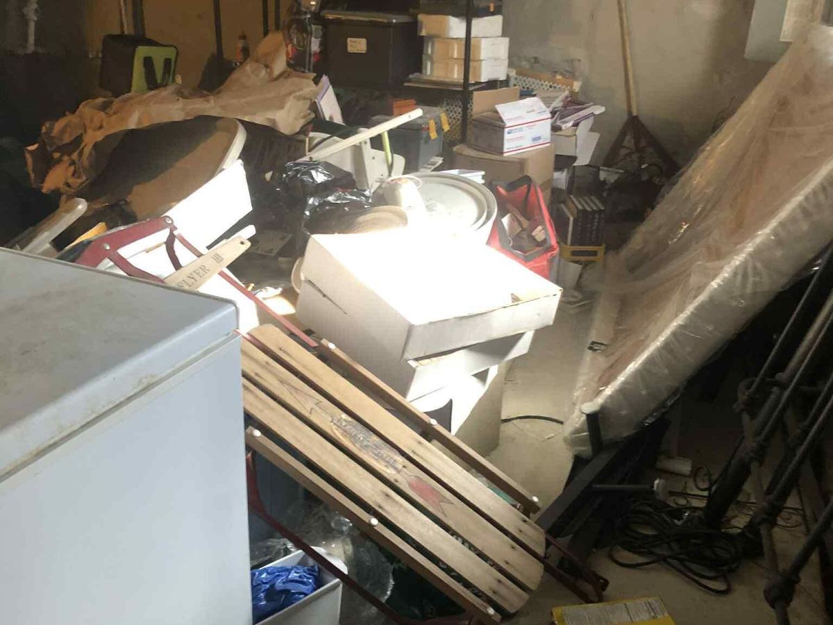 A basement with an old chest freezer, a wooden sled, stacked boxes and a mattress wrapped in plastic